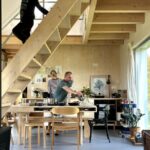 Dieťa schádza po drevenom schodisku nad jedálenským kútom, kde dospelí pripravujú jedlo.