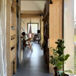 Úzka chodba s vysokými drevenými policami po stranách, šedou podlahou a výhľadom do vzdialenej pracovnej zóny.