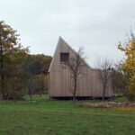 Moderný dom s dreveným obkladom a šikmou sedlovou strechou, obklopený zelenou trávou.
