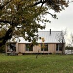 Moderný drevený dom s bielouplechovou strechou a presklenou fasádou na lúke.