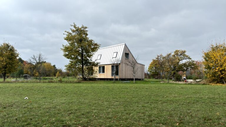 Moderný drevený dom so svetlou šikmou plechovou strechou a strešnými oknami.