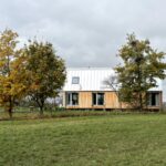 Drevený dom so širokou fasádou, horizontálnymi oknami a plechovou strechou.