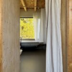 Pohľad do kúpeľne s drevenými obkladmi, OSB stropom a dlhým bielym sprchovým závesom.