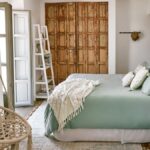 Spálňa v boho štýle s mätovou posteľou, dreveným čelom, ratanovým kreslom a patinovanými dverami.