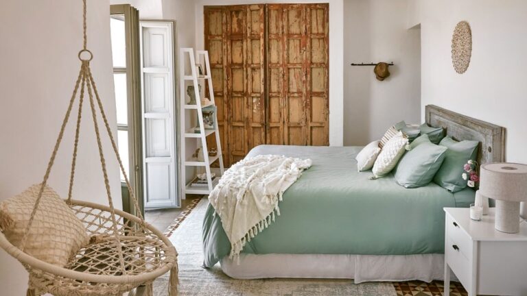 Spálňa v boho štýle s mätovou posteľou, dreveným čelom, ratanovým kreslom a patinovanými dverami.