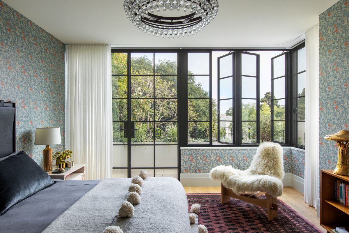 Luxusná spálňa s kvetinovou tapetou, krištáľovým lustrom a veľkými kovovými francúzskymi oknami.