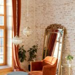 Mäkké kreslo pri tehlovej stene a opretom zrkadle vedľa rastlín.