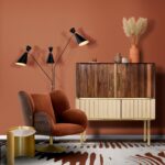 Mäkké kreslo v odtieni terakoty vedľa drevenej retro skrinky a lampy.