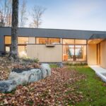 Exteriér moderného domu v jesennej prírode s tmavosivým obkladom a svetlým drevom a kamenným záhradným dizajnom.