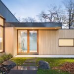 Vchod do domu s presklenými dverami, svetlým dreveným obkladom a chodníkom zo štvorcových dlaždíc.