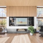 Minimalistická obývacia izba so svetlou drevenou podlahou, integrovaným krbom a veľkými oknami s výhľadom do lesa.