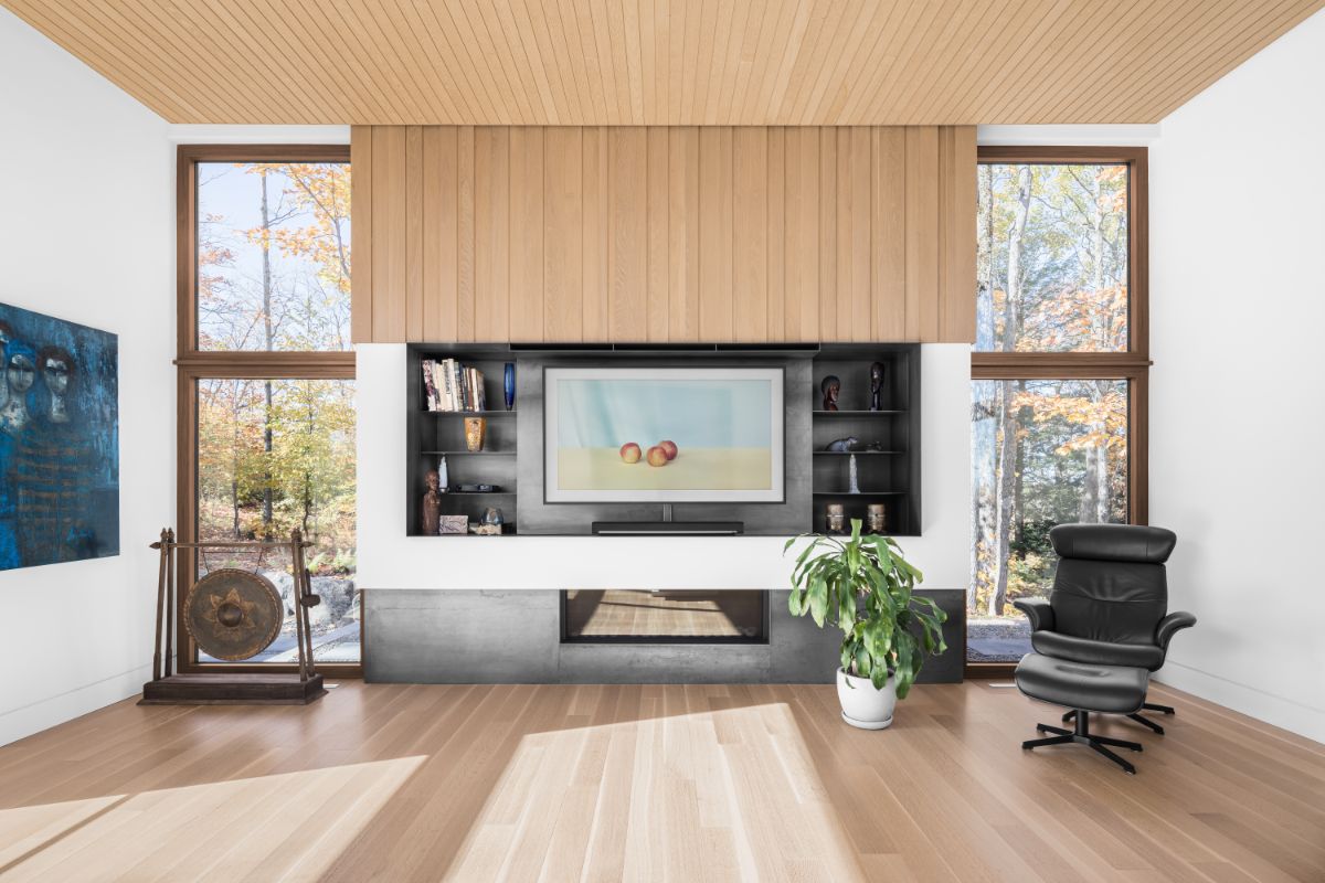 Minimalistická obývacia izba so svetlou drevenou podlahou, integrovaným krbom a veľkými oknami s výhľadom do lesa.