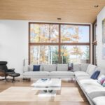 Priestorová obývacia izba so svetlosivou rohovou sedačkou, koženým kreslom a drevenou podlahou pri veľkom okne