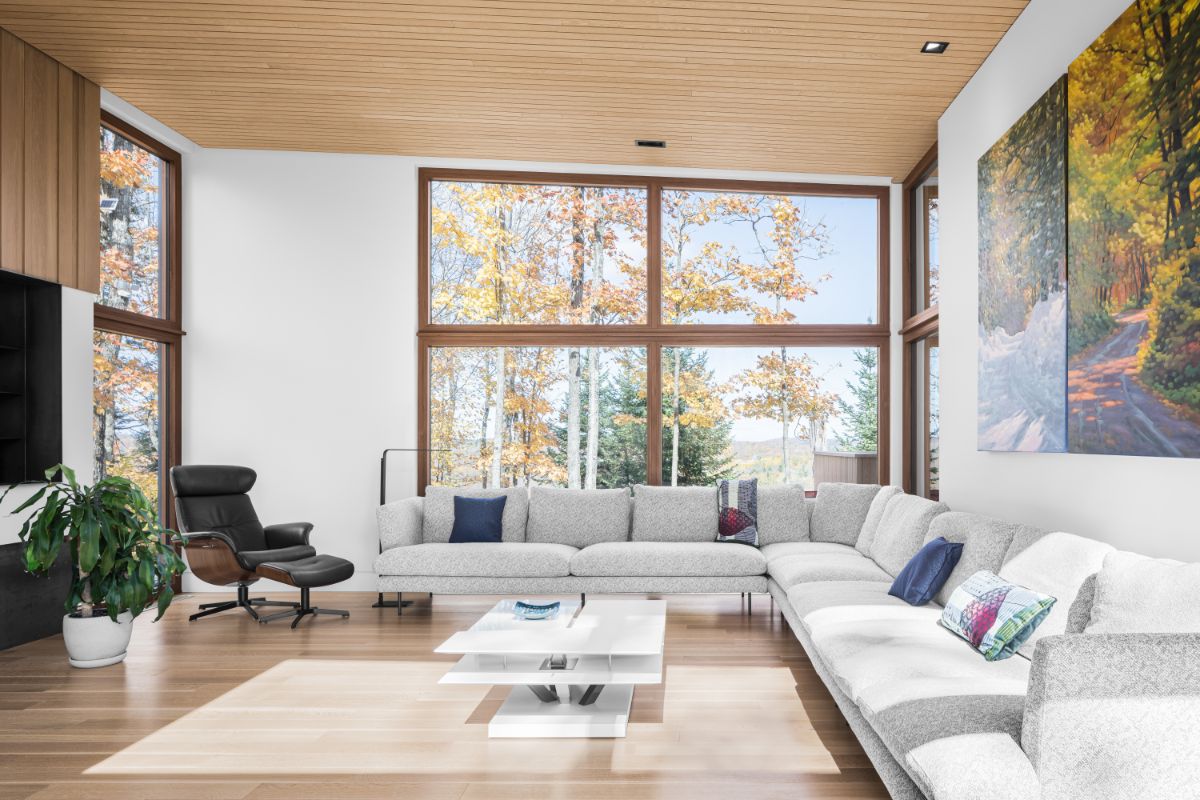 Priestorová obývacia izba so svetlosivou rohovou sedačkou, koženým kreslom a drevenou podlahou pri veľkom okne