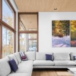 Rohová sedačka v obývačke s drevenou lamelovou stropnou úpravou a veľkými oknami s drevenými rámami.