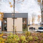Exteriér moderného domu v jesennom prostredí s dreveným a tmavosivým obkladom a vonkajšou terasou.