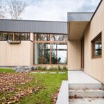 Moderný exteriér domu s fasádou z vertikálneho dreveného obkladu, tmavou strechou a veľkými okennými plochami.