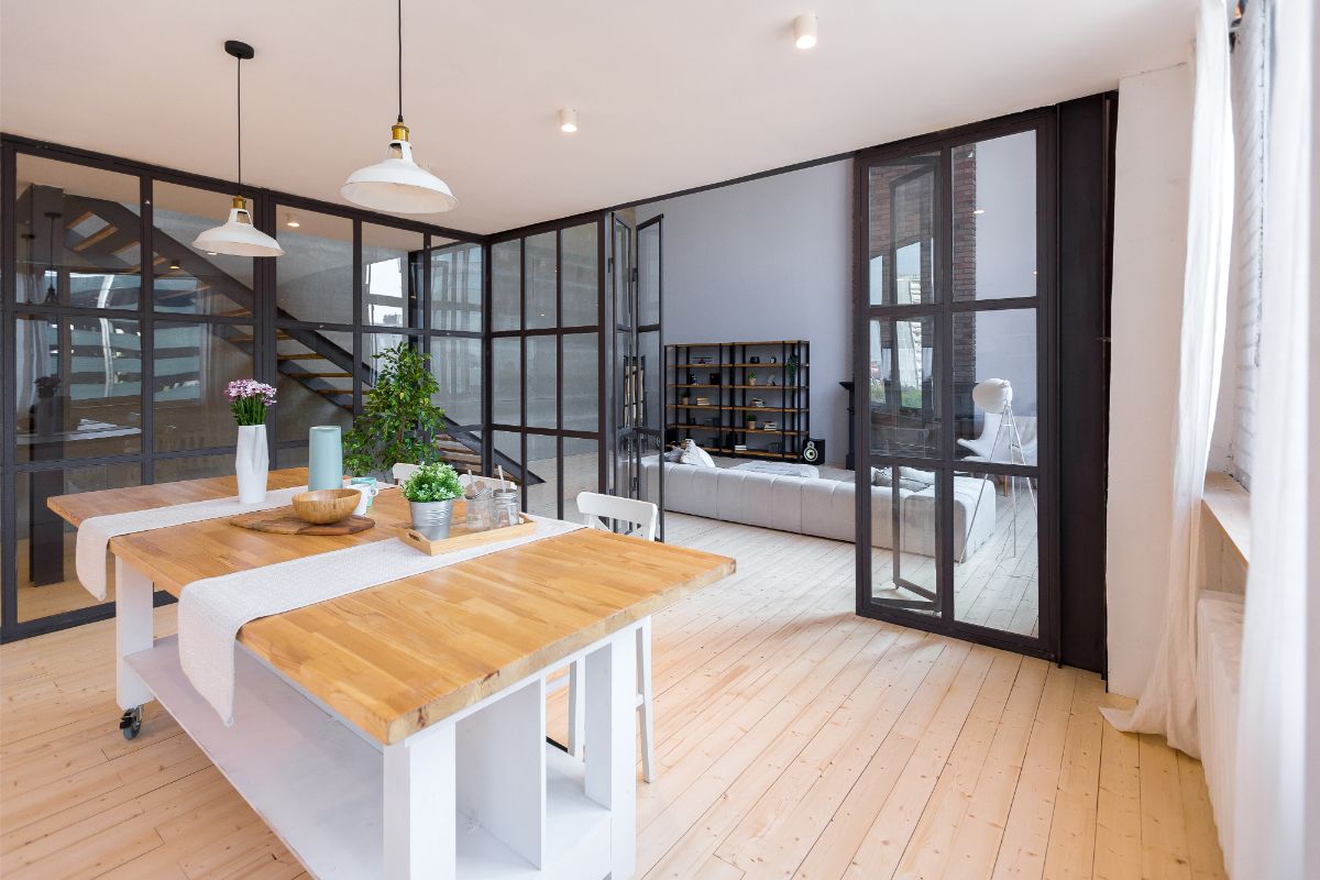 Pohľad z jedálne s jedálenským stolom do obývačky, oddelenej sklenenou priečkou so skladacími dverami.
