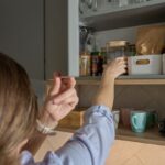 Žena vyberá premet z kuchynskej skrinky.