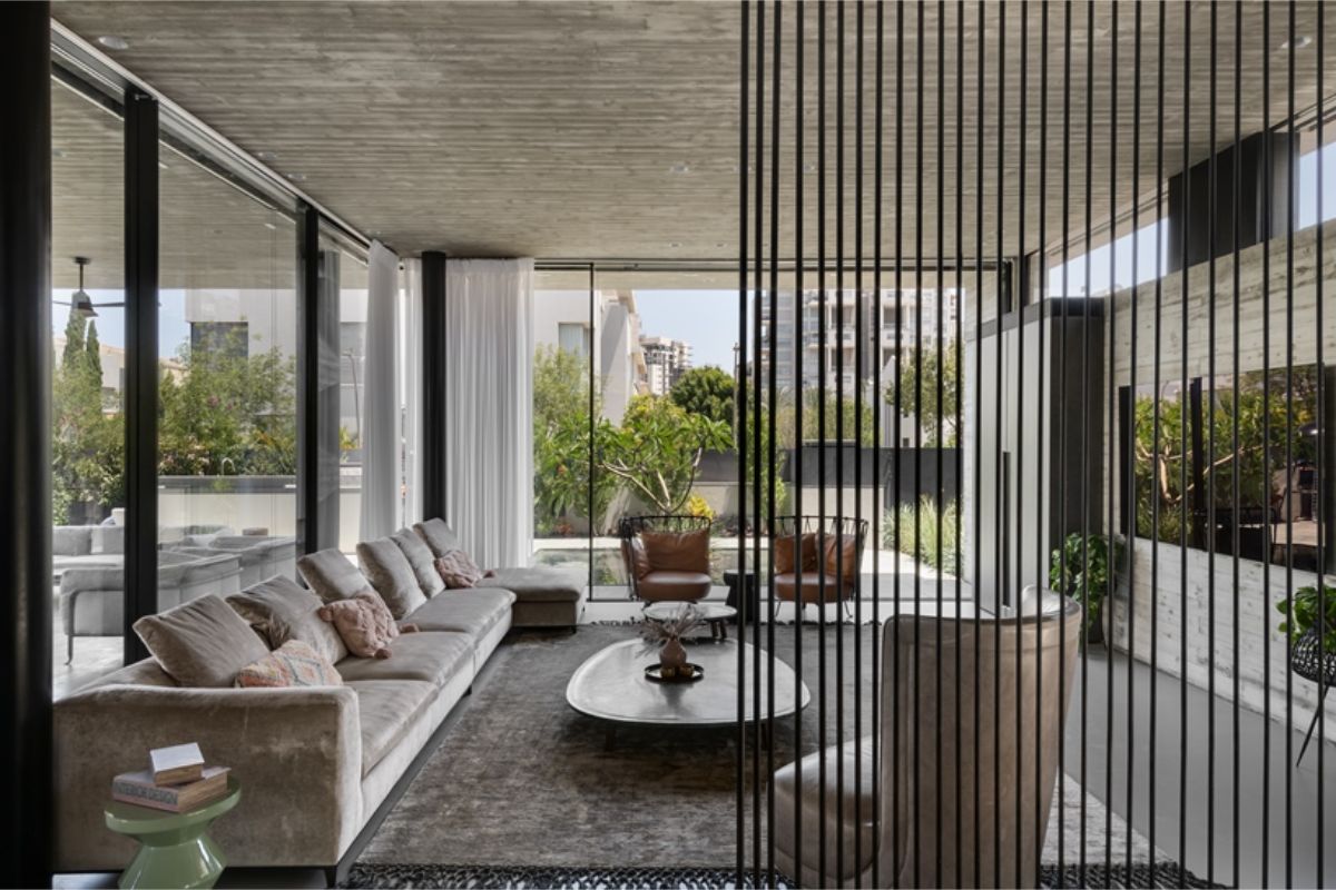 Luxusná moderná obývacia izba s béžovou zamatovou sedačkou, betónovým stropom a vysokými presklenými oknami do záhrady.