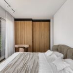 Svetlá spálňa s bielou omietkou, drevenou skriňou a posteľou so zamatovým čelom a s priamym vstupom na terasu.