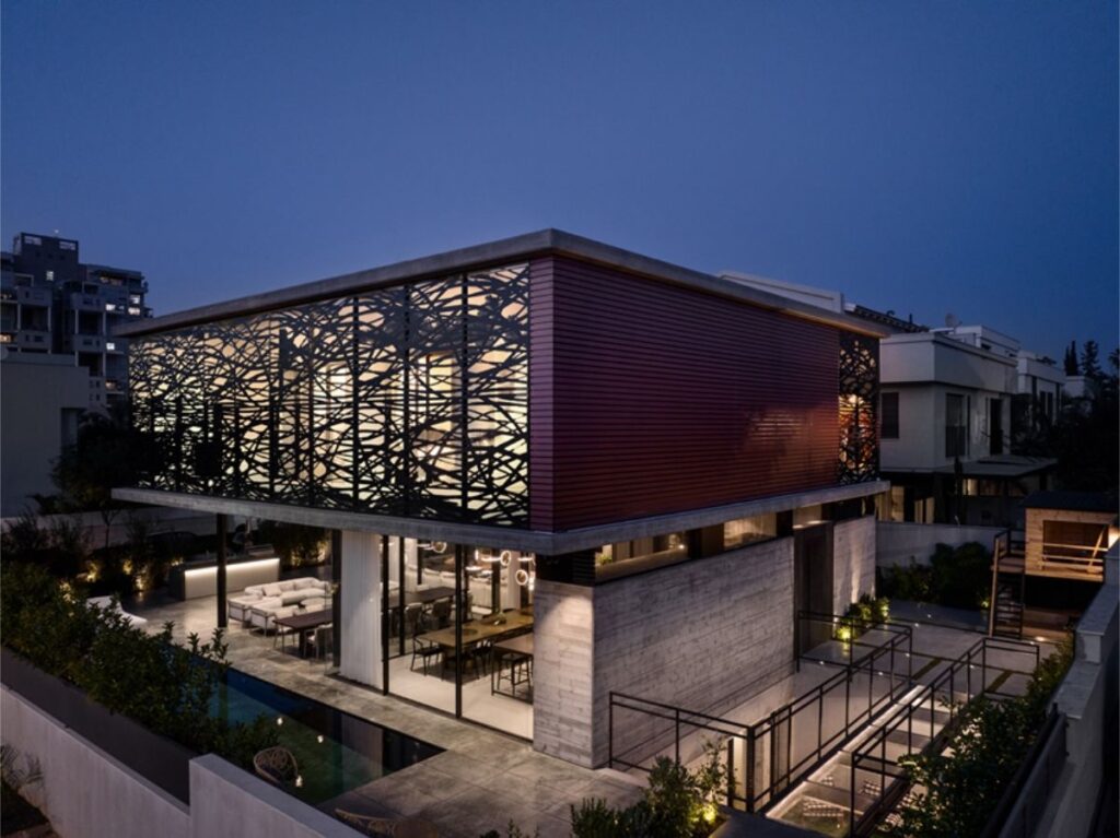 Moderná architektonická vila v noci s výrazným červeno-hnedým obkladom a dekoratívnymi lamelami na hornom podlaží.