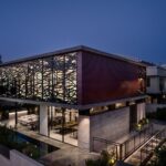 Moderná architektonická vila v noci s výrazným červeno-hnedým obkladom a dekoratívnymi lamelami na hornom podlaží.