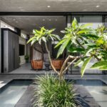 Moderný exteriér s vodným prvkom a zeleňou, z ktorého vidieť do interiéru.