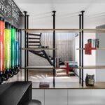 Interiér s modernou drevenou knižnicou s kovovými stĺpmi a veľkými farebnými nádobami na stene.