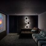 Luxusná domáca kinosála s tmavým čalúneným kobercom, modro-čiernou sedačkou a kruhovým LED osvetlením na stene.