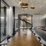 edáleň s dlhým kovovým stolom, čiernymi stoličkami a nápaditými zlatými závesnými svietidlami pod betónovým stropom.