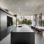 Minimalistická čierna kuchyňa s integrovanými spotrebičmi a veľkým ostrovčekom s výhľadom na jedáleň a bazén.