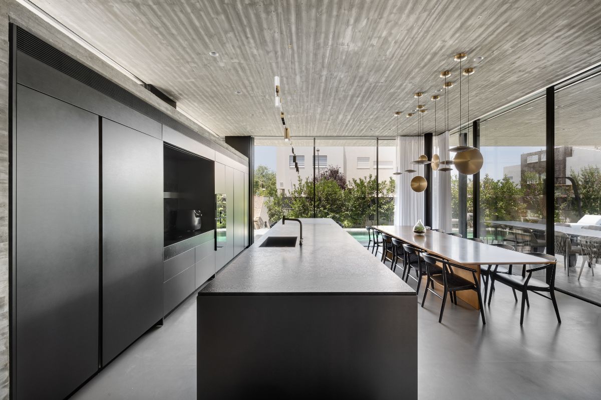 Minimalistická čierna kuchyňa s integrovanými spotrebičmi a veľkým ostrovčekom s výhľadom na jedáleň a bazén.