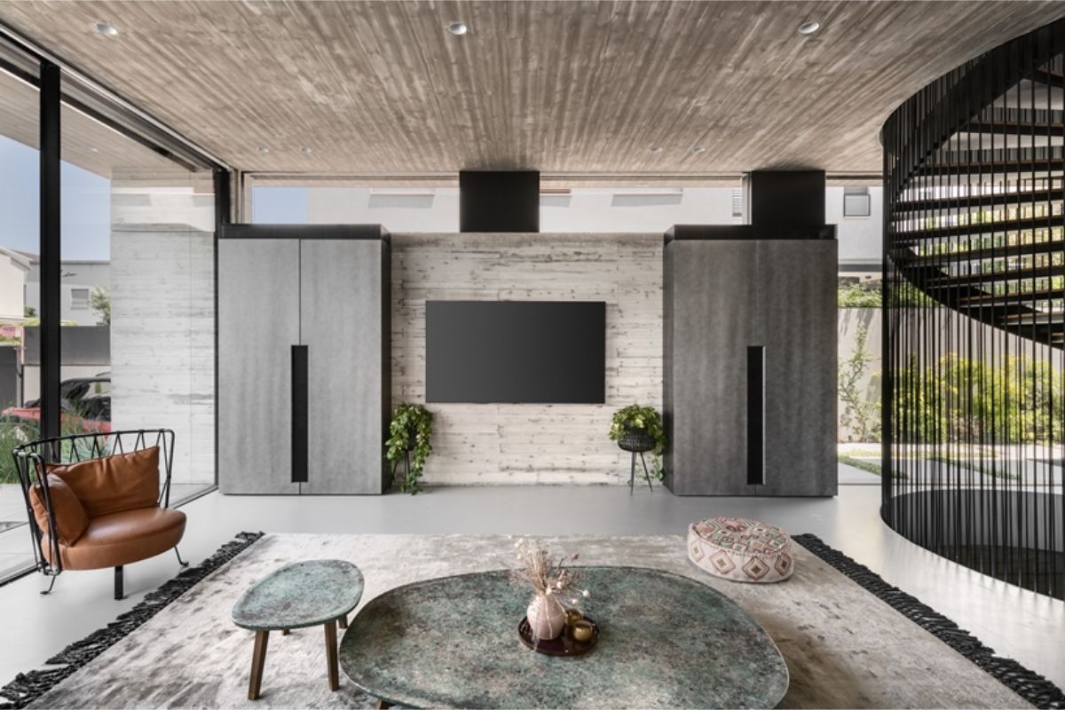 Moderná spoločenská miestnosť s betónovými stenami a stropom, koženým kreslom a kovovými odkladacími stolíkmi v zelenej farbe.