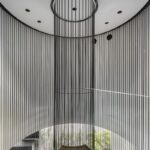 Centrálne točité schodisko s drevenými schodnicami a vysokými kovovými lamelami, vytvárajúce vertikálnu čiernu dominantu.