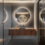 Luxusná kúpeľňa s tmavou betónovou stenou, obkladom zo zeleného mramoru a okrúhlym zrkadlom s LED osvetlením.