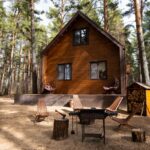 Moderná chata obložená drevom v tradičnom tvare s terasou a ohniskom so sedením.