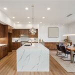Moderná kuchyňa s tmavým dreveným obložením, bielym ostrovčekom s mramorovou textúrou a jedálenským kútom.