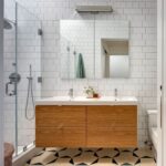 Kúpeľňa s dvojitým dreveným umývadlom, bielymi obkladmi v tvare metro a vzorovanou podlahou v čierno-béžovej farbe.