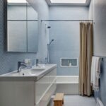 Moderná kúpeľňa s bledomodrými mozaikovými dlaždicami, bielym dvojumývadlom a vaňou.