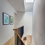 Schodisko a chodba s drevenou podlahou, čiernym kovovým zábradlím a strešným oknom.