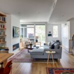 Priestorná otvorená obývačka s drevenou podlahou, sivou sedačkou a vstavanými drevenými policami.