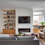 Obývacia izba s bielymi stenami, vstavaným krbom, TV a otvorenými drevenými policami plnými kníh.