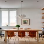 Jedáleň s dreveným stolom a kombináciou čiernych, drevených a chrómových stoličiek pod bielym lustrom.