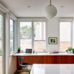 g Domáca kancelária pri veľkých oknách s drevenými skrinkami a bielou pracovnou plochou.