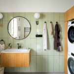 Moderná kúpeľňa so svetlozeleným obkladom, kruhovým zrkadlom, drevenou skrinkou pod umývadlo a spotrebičmi.