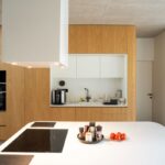 Kuchynský ostrov s indukčnou doskou a biela kuchynská linka v drevenom dubovom obklade s betónovým stropom.