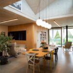 Moderný jedálenský kút s dreveným stolom, farebnými stoličkami a dizajnovým osvetlením pod priznaným betónovým stropom.