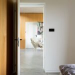 Pohľad cez otvorené dvere do obytnej miestnosti s dreveným obkladom a bielou knižnicou.