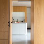 Pohľad cez otvorené dvere do minimalisticky zariadenej kuchyne.